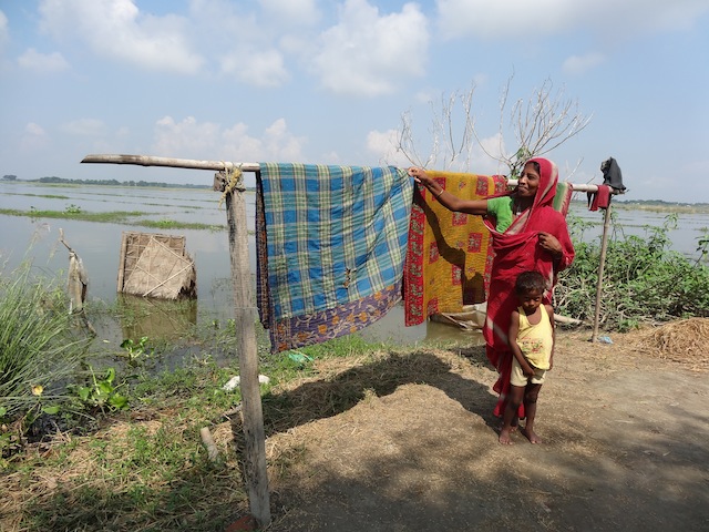A woman dries blankets after her home went underwater for five days in one of the villages of the Morigaon district. The woven bamboo sheet beyond the clothesline used to be the walls of her family's toilet. August rains inundated 141 villages in the district. Credit: Priyanka Borpujari/IPS