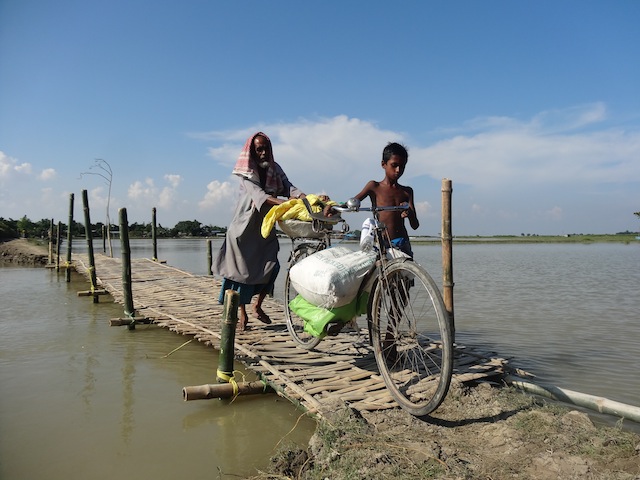 In places where roads have collapsed, the government has erected bamboo bridges. When the government is absent, locals do this work themselves. This man and child travel from one village to another on a boat, and travel by foot over the bridges. Credit: Priyanka Borpujari/IPS