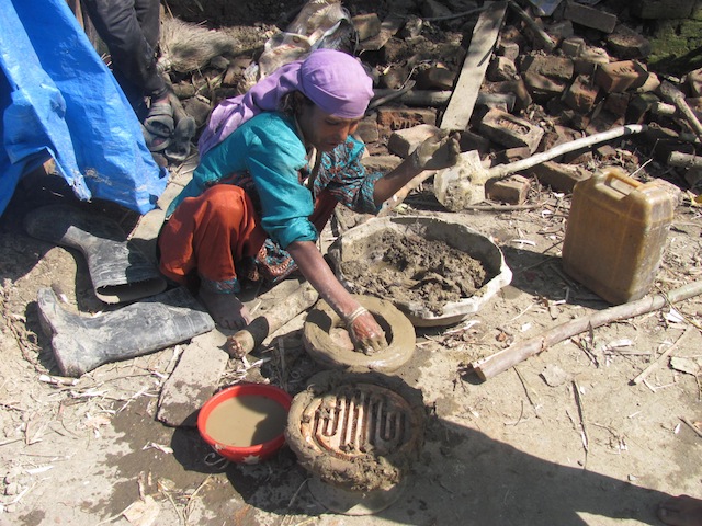 Hajira Begam, a 49-year-old flood victim, rigs up a clay cover for an electric coil that will serve as her stove in the absence of a proper home and kitchen. Credit: Athar Parvaiz/IP