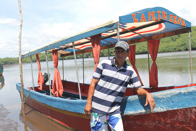 Carlos Menjívar, standing next to his boat La Princesa on the Barra de Santiago estuary on El Salvador's Pacific coast, says the buildup of sediment has made it impossible at times to navigate in the channels because they are too shallow. Credit: Edgardo Ayala/IPS