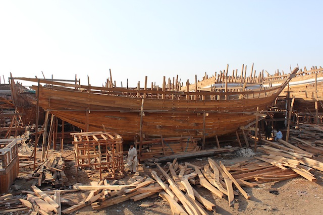 A fisherman walks in front of one of the many half-constructed wooden arks that lie strewn about the Karachi harbour. Credit: Zofeen Ebrahim/IPS