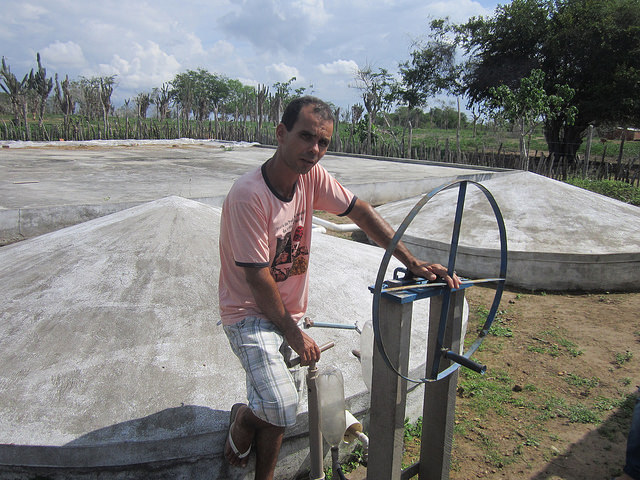 Abel Manto stands next to the closed water tanks built to collect rainwater and irrigate his vegetable gardens in the Northeastern Brazilian state of Bahia. The green on this farmer and inventor's land stands in sharp contrast with the aridity of the region, while the lids on his tanks keep mosquitoes from breeding in the water. Credit: Mario Osava/IPS