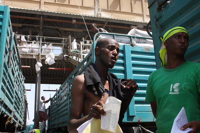 Port workers, including Agaby (right), make the most of what shade is available between trucks being filled with food aid destined to assist with Ethiopia's ongoing drought. Credit: James Jeffrey/IPS