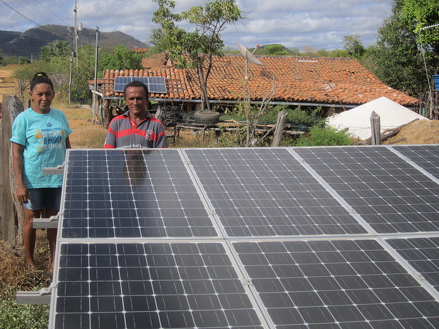 Local farming couple Marlene and Genival Lopes dos Santos stand next to solar panels that are part of community-shared generation, which reduces their electricity bill and those of their urban partners, who live in the cities of Sousa and João Pessoa, capital of the state of Paraiba, 400 km away, in Brazil's Northeast. Credit: Mario Osava/IPS