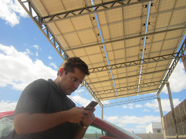 Entrepreneur Paulo Gadelha uses his cell-phone under the solar panel rooftop covering part of the truck park area at his poultry slaughterhouse. Thanks to solar energy, Gadelha reduced electricity costs to zero in the slaughterhouse, a dairy plant, a store and his family's home in the Brazilian municipality of Sousa, in the northeast of the country. Credit: Mario Osava/IPS
