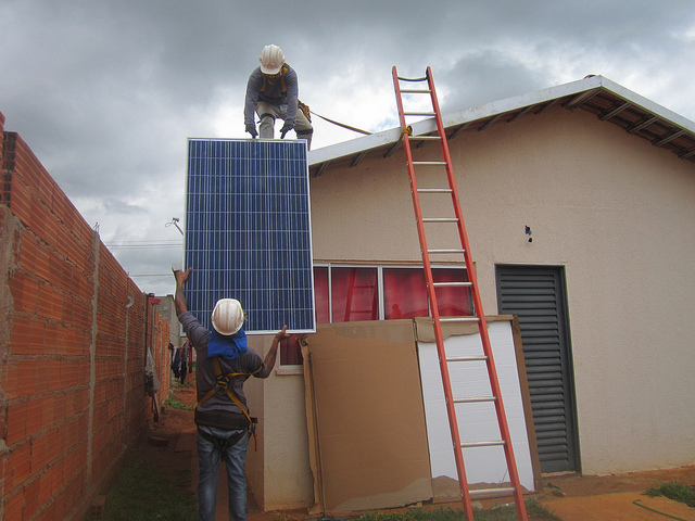 Two workers install solar panels on a house in the Maria Pires Perillo housing complex, an additional benefit for the poor families who are buying their homes at a very low cost. The Goiana Housing Agency of the state government of Goias, in central Brazil, subsidises most of the housing and the solar energy. Credit: Mario Osava/IPS