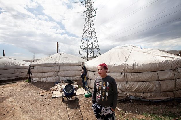 A woman stands outside a yurt in Ger District, Ulaanbaatar, Mongolia. There is power plant nearby but the government says it aims to reach net-zero emissions by 2050. Courtesy: CC BY-SA 4.0/Nathalie Daoust