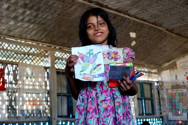 A Rohingya girl proudly holds up her drawing at a UNICEF school at Balukhali camp, Bangladesh.As Rohingya refugee families settled in the Cox’s Bazar Kutupalong Refugee Camp, the area had one of highest rates of primary and secondary age children out of school. Education Cannot Wait (ECW), the multilateral global fund dedicated to education in emergencies and protracted crises, immediately allocated US$3million to urgently scale up learning spaces for displaced Rohingya children. In 2018, the Fund increased its support with an additional US$12 million for the continuous learning of refugee and host community children. (file photo) Credit: Farid Ahmed/IPS