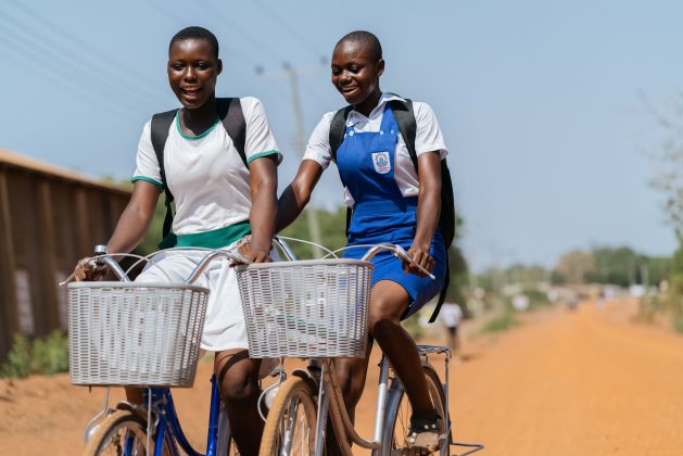 Sarah og Doris sykler til skolen fordi de bor flere kilometer unna.  Ghanas utdanningssektor var en av de hardest rammede av pandemien, og for mange jenter, spesielt de i landlige områder, betyr konsekvensene av nedleggelse av skolen at mange aldri kommer tilbake til skolegangen.  Kreditt: Jamila Akweley Okertchiri / IPS