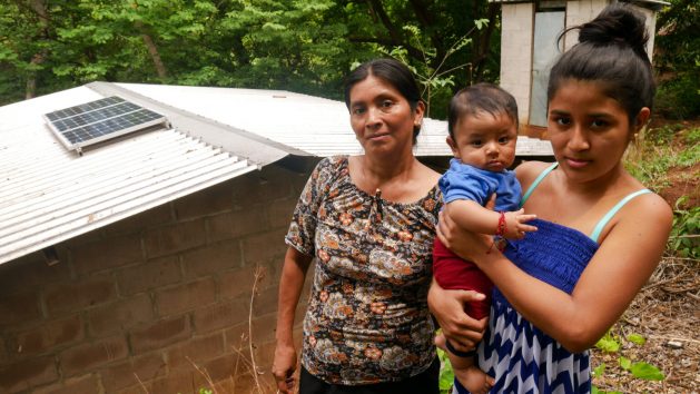 Francisca Piecho stands with her daughter-in-law Johana Cruz and her grandson outside her home that now has electricity from solar energy, in the village of Cacho de Oro, Teotepeque municipality, in the southern department of La Libertad. Hers and other rural Salvadoran families have seen their lives improve with the arrival not only of electricity but also of a reforestation program in the area. CREDIT: Edgardo Ayala/IPS
