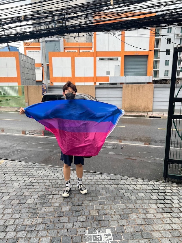   Junwoo Na, LGBTQ topluluğuna desteğini göstermek için Bangkok'ta sokakta bir gurur bayrağı tutuyor.  Kredi bilgileri: Junwoo Na/IPS