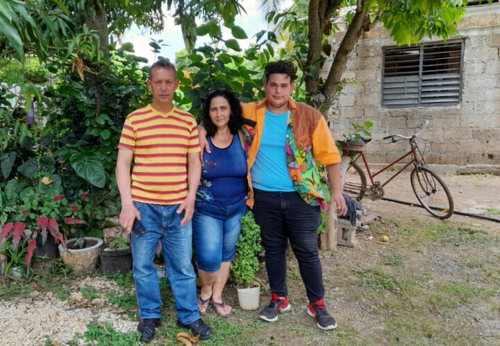 Mayra Rojas, her husband Edegni Puche and the couple's youngest son stand in the backyard of their home. Family support for household chores, cleaning the yard and caring for the family's animales, along with increased awareness of environmental care are other benefits that the biodigester has brought to the life of this rural Cuban woman. CREDIT: Jorge Luis Baños/IPS
