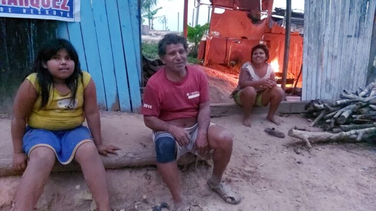 Sentado frente a su casa en Neshulla, en la región amazónica peruana de Ucayali, se encuentran el agricultor Úber Paredes y dos de sus hijas.  Delia, a la derecha, se vio obligada a abandonar la escuela después de quedar embarazada y su padre no podía permitirse comprar sus útiles.  Ahora con 17 años, no ha olvidado su deseo de convertirse en enfermera.  Su hermana Alexandra, a la izquierda, prometió apoyarla en el futuro.  CRÉDITO: Gladys Galarreta/ IPS