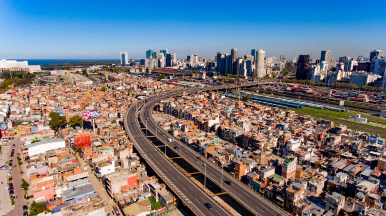 Aerial view of the Padre Mugica neighborhood, or Villa 31, as many still call it, with downtown Buenos Aires in the background. The 90-year-old informal settlement now straddles a freeway and has more than 40,000 inhabitants, just minutes from the heart of the Argentine capital. CREDIT: City of Buenos Aires
