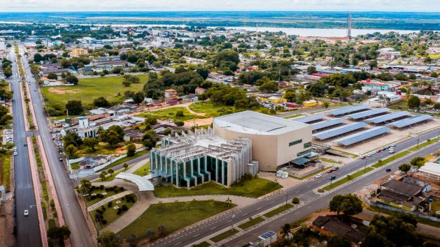 Aerial view of the Municipal Theater of Boa Vista and its parking lot covered by solar panels, near the center of a city of wide avenues, empty spaces, abundant solar energy and high quality of life compared to other cities in Brazil’s Amazon region. In the background is seen the Branco River, which could be dammed 120 kilometers downstream for the construction of a hydroelectric plant that would flood part of the capital of the state of Roraima. CREDIT: Boa Vista city government