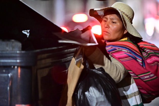 Sofía Quispe, the president of Ecorecicladoras de La Paz, finds a good haul of paper and cardboard in a municipal dumpster at the end of Avenida 6 de Agosto in La Paz, in a nighttime job that the southern hemisphere winter makes more challenging. CREDIT: Franz Chávez / IPS