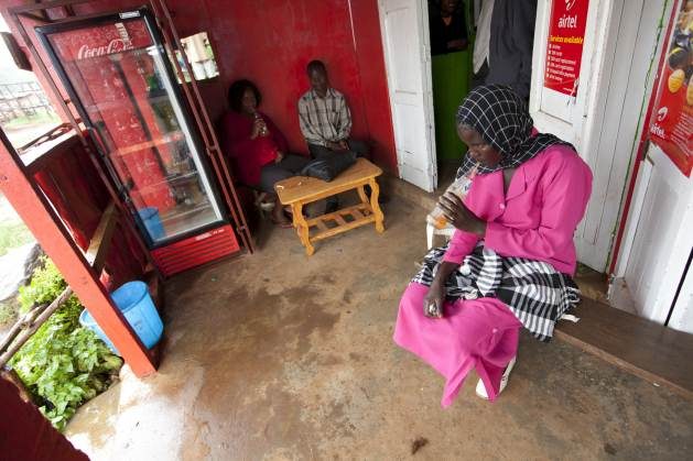 Young woman sips an orange soda and waits for the rain to stop, on the porch of a small country store in a rural village in Bungoma County, Kenya. Credit: IFAD/Susan Beccio.