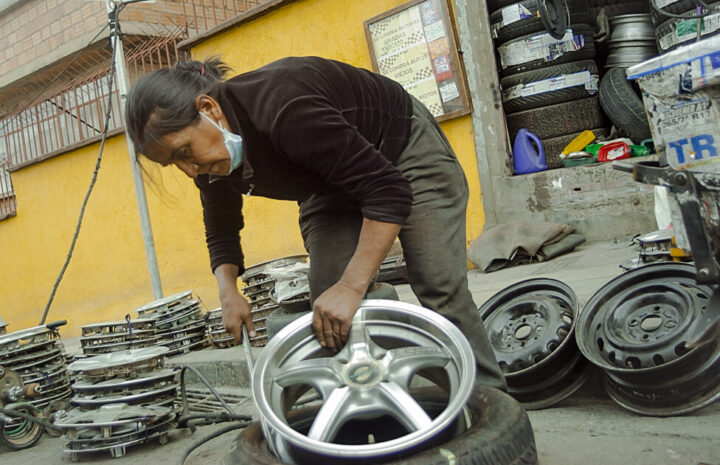 Ana Castillo vérifie l'une de ses jantes sur le trottoir de son atelier, dans une rue animée du quartier de Sopocachi, dans la ville bolivienne de La Paz.  La mécanique automobile n'a pas de mystère pour Castillo, qui est également spécialiste de la reconstruction de voitures anciennes.  CRÉDIT : Franz Chávez / IPS