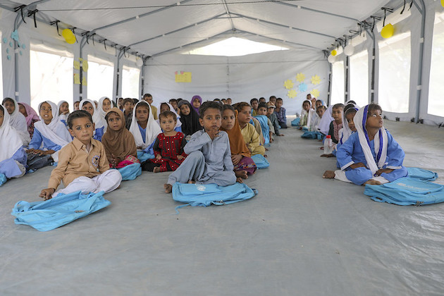 Young girls and boys after receiving bags, books and copies from UNICEF attend their first class at a UNICEF-supported temporary learning center next to floodwaters in the village of Allah Dina Channa, Lasbela district, Balochistan province, Pakistan.  The primary school was severely damaged during heavy monsoon rain in 2022. Credit: UNICEF