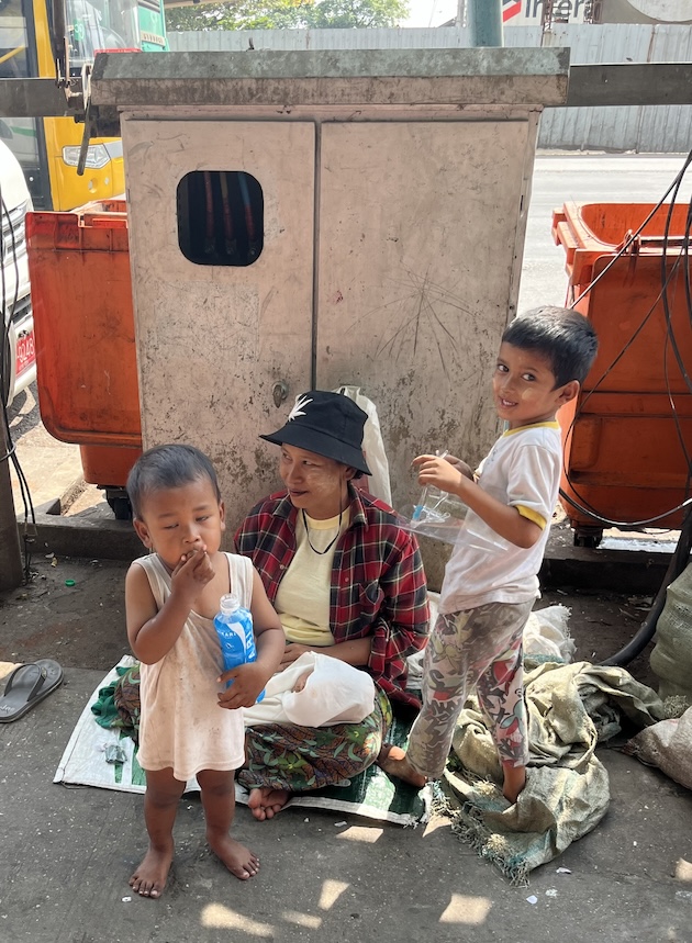 A woman with two toddlers and a baby on her lap beg outside a temple in Yangon. People say more children can be seen begging these days as the economy struggles and migrants move into the city from conflict areas. Credit: William Webb/IP