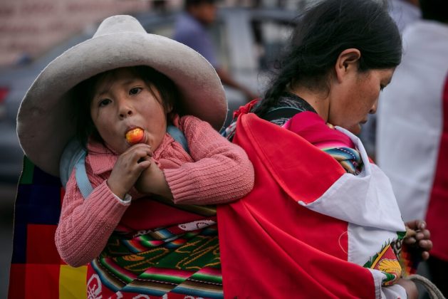 A young Quechua mother, originally from Peru's southern Andes highlands, walks through the streets of Lima, carrying her young daughter in her lliclla (a colorful shawl made by native women in the Andes). A quarter of Peru's rural population under the age of five suffers from chronic malnutrition, clear evidence of inequality, which will have severe impacts on the rural child population. CREDIT: Wálter Hupiú / IPS