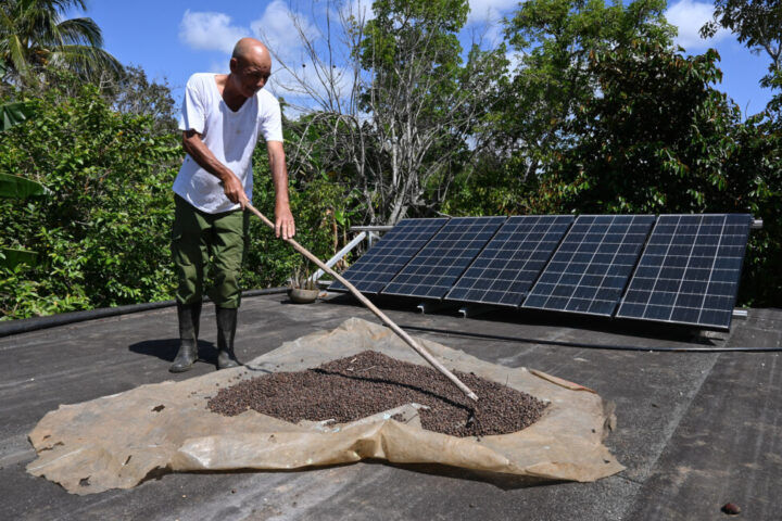 Alexis García suší kávové zrná vedľa solárnych panelov inštalovaných na streche svojho domu v južnej Havane.  Možnosť uskladnenia energie so získanou záložnou batériou poskytuje rodine približne tri hodiny autonómie počas výpadku prúdu.  Poďakovanie: George Louis Bains / IPS