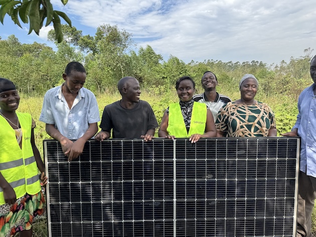 Shifra Ainomugisha (centre, in reflective vest), co-founder and CEO of Solar Farm Uganda, stands with farmers and community members beside a solar panel installation supporting climate-smart agriculture initiatives. Through renewable energy and farmer-centred innovation, the project seeks to reduce food loss and improve rural incomes. Credit: Solar Farm Uganda